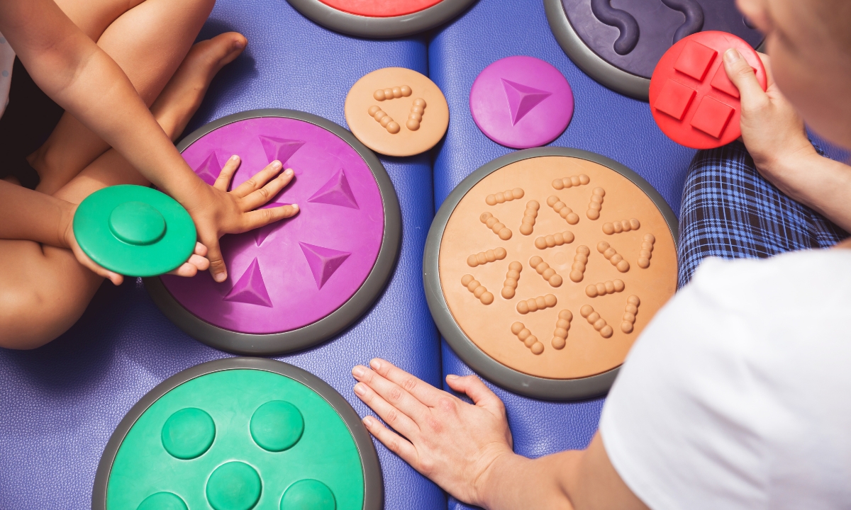 a mat of sensory toys, two children's hands playing with them